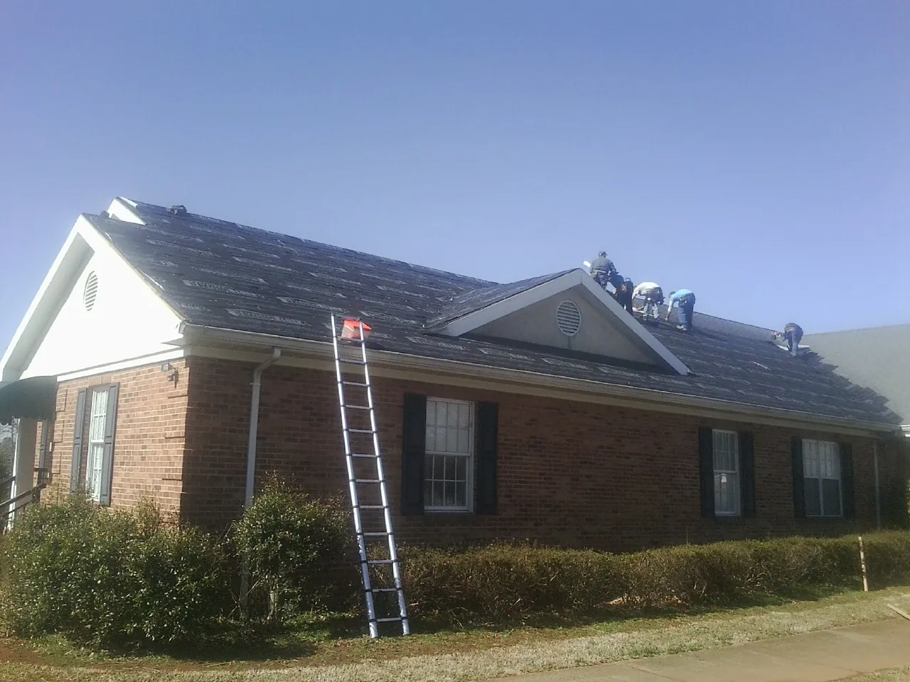 Crew tearing shingles off a brick ranch roof with a ladder set — Metal Roof Repair work by our crew in Woodruff