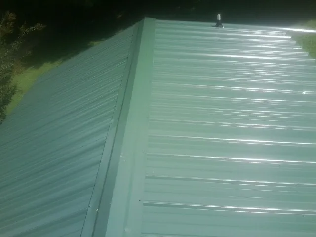 New green metal panels meeting at the ridge of a roof — Flat Roof Repair work by our crew in Woodruff