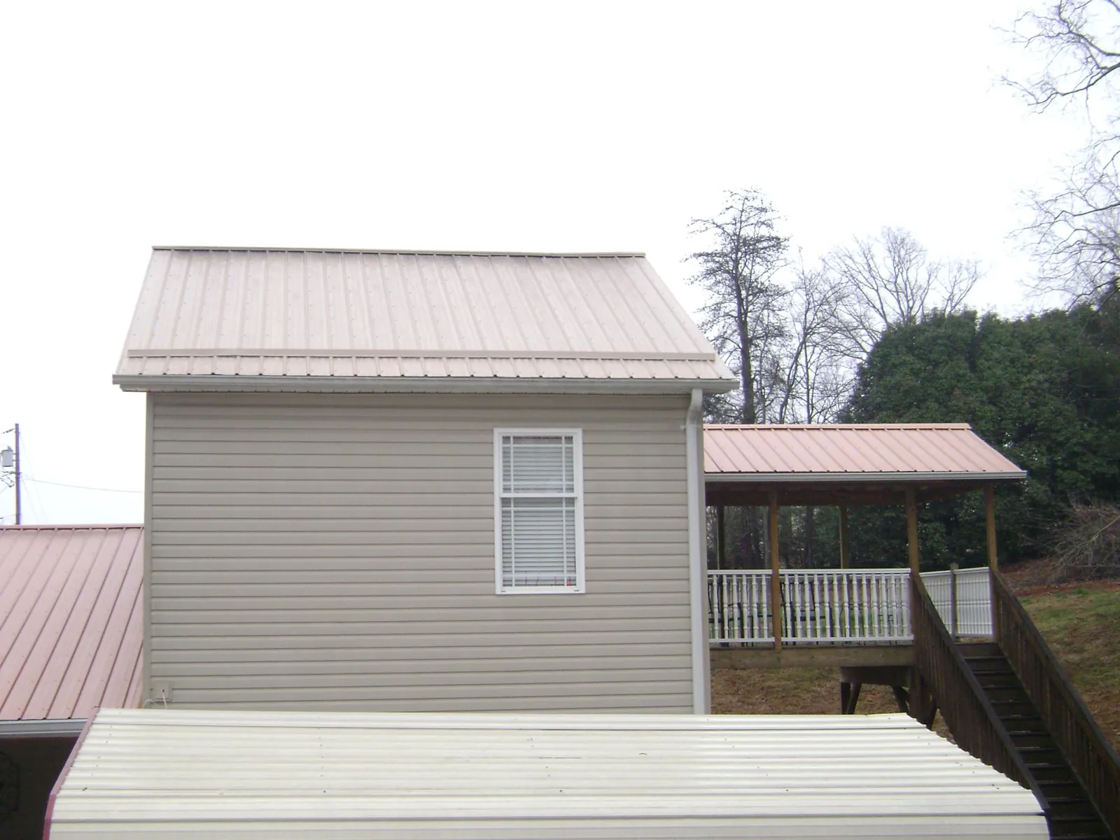 Tan metal roofs on a two story addition and attached porch, from a Roof Replacement job in Woodruff